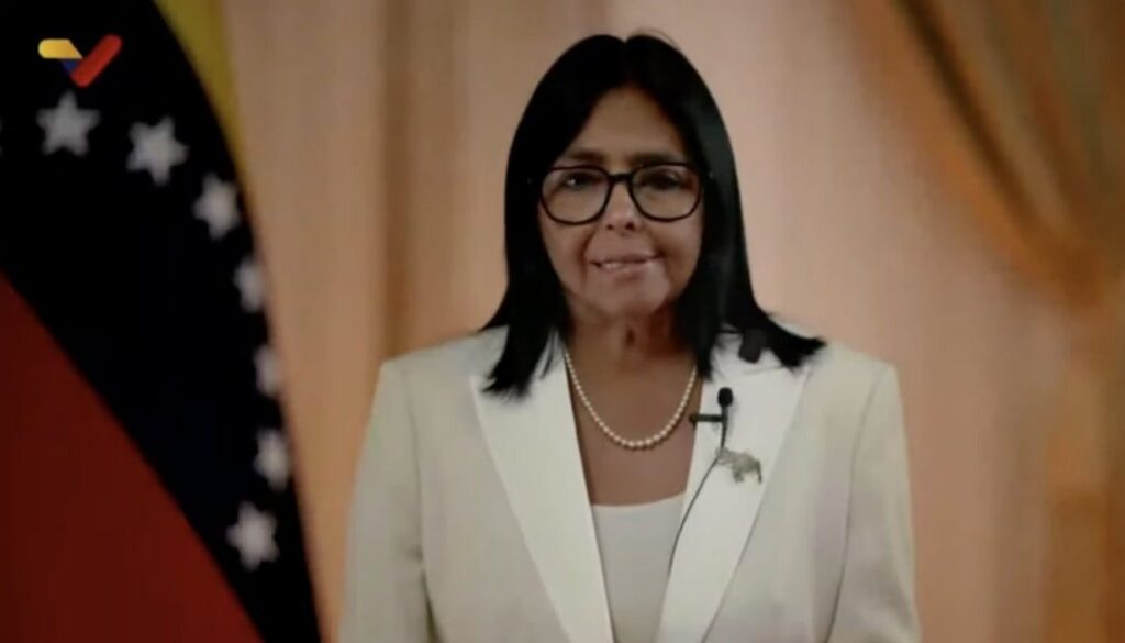 La presidenta encargada Delcy Rodríguez, con chaqueta blanca, durante su alocución transmitida por VTV, junto a la bandera de Venezuela.