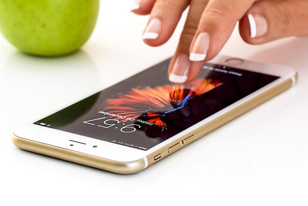 Dedo que toca la pantalla de un teléfono móvil sobre una mesa blanca.
