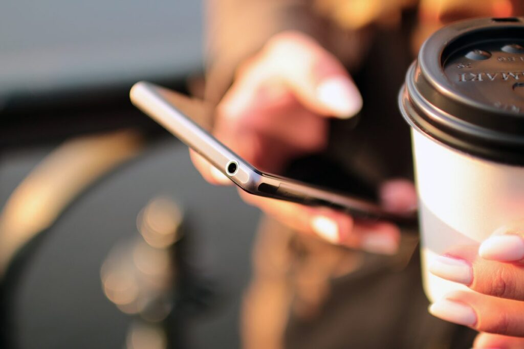 Manos que usan un teléfono móvil junto a un vaso de café.